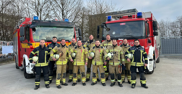 Gruppenbild Gruppenbild der Lehrgangsteilnehmer mit Einsatzkleidung, die vor zwei Feuerwehrfahrzeugen stehem
