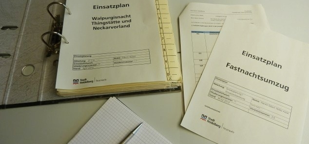 Einsatzplanung offener Leitzordner mit einem Einsatzplan, daneben ein Block mit Kugelschreiber